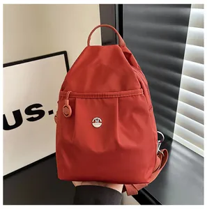 Detail shot of lightweight brick-red nylon backpack with M metal charm and fashion logo