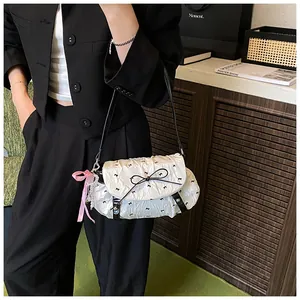Detail of white pleated bag with black bows and pink checkered charm on strap