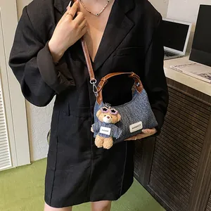 Blaue Denim-Halbmondtasche mit Lederriemen und Plüschbär-Anhänger am Modell