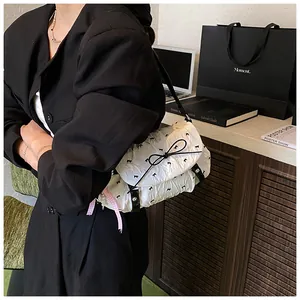 Close-up of white crossbody bag with bow embroidery, pearl charm and black strap
