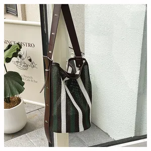 Detalle de bolso saco de malla a rayas con correa ajustable de cuero marrón oscuro