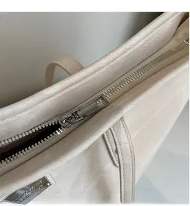 Detail view of smooth silver metal zipper and brand logo plaque on beige canvas tote bag