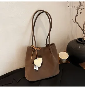 Detail of suede tote bag featuring a leather bow and white plush heart pendant accessory
