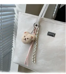 Close-up of a plush teddy bear bag charm with woven rope knots on a white tote bag