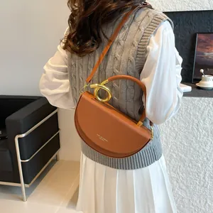 Brown semi-circular saddle bag with golden circular metal handle and thin shoulder strap