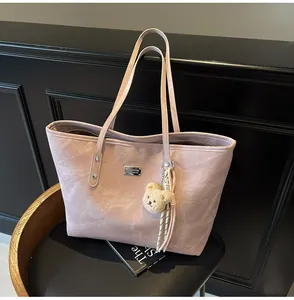 Close-up of pink suede tote bag featuring silver logo and a brown plush bear charm