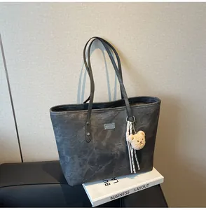 Detail of dark gray tote bag texture with plush bear charm and metallic logo on a book