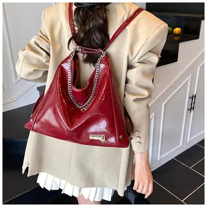 Detail of red patent leather triangular backpack with bold silver chain and metal plate