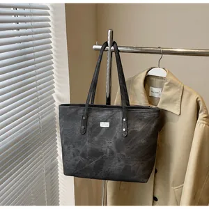 Detail of dark gray tote bag with metallic plate hanging against a khaki trench coat