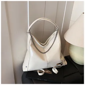 Detail view of cream hobo bag with silver chain and heart padlock on a leather surface