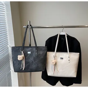 Close-up of grey and beige textured tote bags featuring metal logo and plush bear charm