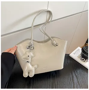 Detail einer hellgrauen Lackleder-Tote mit Giraffenanhänger und geknoteten Riemen