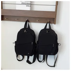 Detalle de dos mochilas de nailon impermeable negro colgadas en un gancho de pared blanco