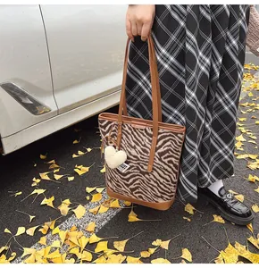 Close-up of zebra pattern bucket bag featuring a white heart plush keychain on leather strap