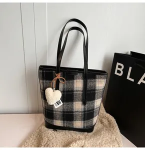 Detailed view of black and white plaid tote bag with heart charm on a soft rug