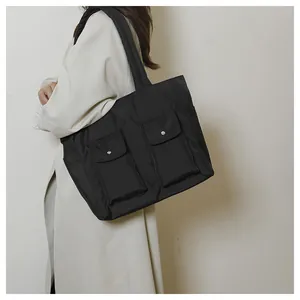 Detail of large black canvas tote bag showing front utility pockets and side pocket
