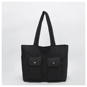 Close-up of black canvas tote bag with dual front flap pockets and silver metal buckles