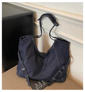 Detailed close-up of dark blue denim tote bag featuring white contrast stitching and buckles
