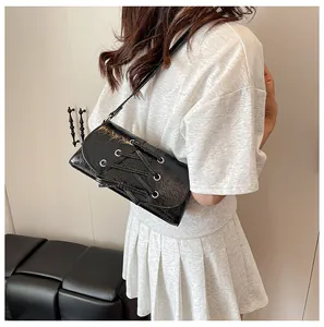 Detail of black patent leather crossbody bag with lace-up eyelets and silver hardware