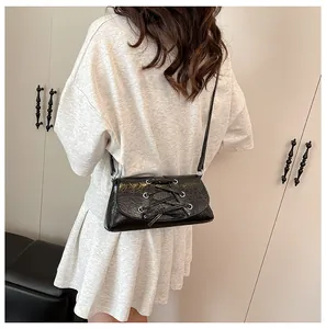 Rear view of model wearing a black lace-up crossbody bag with metallic eyelet details