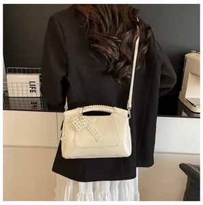 Detailansicht der beigen Beuteltasche mit Spitzenschleife und Herzanhänger am Model