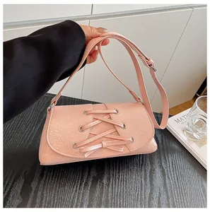 Detail of pink crossbody bag with lace-up design and silver eyelets on a wooden table