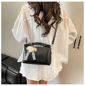 Detail der schwarzen Bucket Bag mit Perlen-Schleife und Spitze auf weißem Outfit