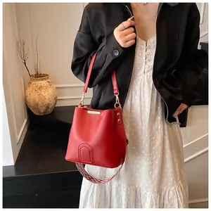 Detail of red bucket bag with wide jacquard strap and minimalist leather shield patch