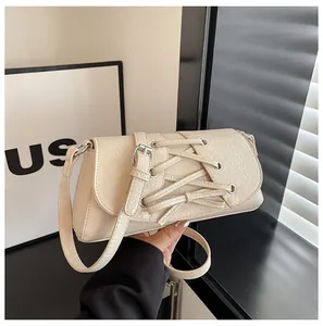 Close-up of off-white bow crossbody bag with silver eyelets and pleated leather texture
