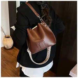 Detail of dark brown leather bucket bag with geometric patterned wide strap and gold hardware