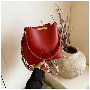 Detail of red bucket bag with gold hardware and stylish wave pattern wide shoulder strap