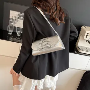Chic silver metallic crossbody bag with lace-up bow detail worn by model in a black blazer