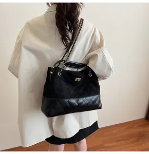 Detail of black quilted tote bag with suede panel and gold metal chain shoulder strap