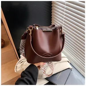 Close-up of dark brown bucket bag featuring a patterned wide shoulder strap and gold hardware