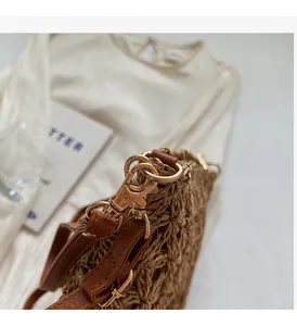 Close-up of golden metal hooks and brown leather strap on a woven straw tote bag