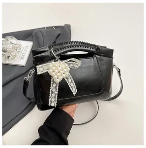 Detail der schwarzen Beuteltasche mit Flechtgriff und Perlen-Spitzen-Schleife auf grau