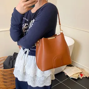 Brown bucket bag with wide strap and gold hardware shown in a casual lifestyle setting