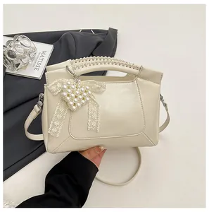 Detail der cremefarbenen Beuteltasche mit Spitzenschleife und Perlenherz-Anhänger