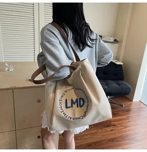 Detail of canvas tote bag with brown leather straps and blue embroidered circular logo