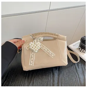 Detail der beigen Beuteltasche mit Perlenherz-Anhänger und Spitzenschleife auf Holztisch