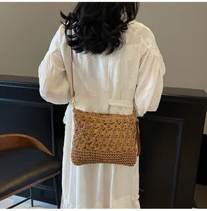 Detail of hand-woven straw tote bag with brown leather strap and intricate cutout patterns