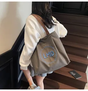 Detailed view of large canvas tote bag with leather straps and blue embroidery detail