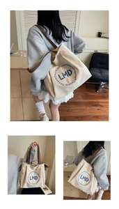 Detail of canvas tote bag with blue letter embroidery and sturdy brown shoulder straps