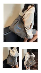 Detail of grey canvas tote bag with blue LMD embroidery and brown shoulder strap