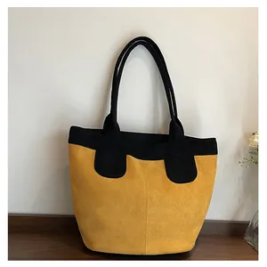 Dettaglio di una grande borsa tote in pelle scamosciata gialla con manici neri su legno