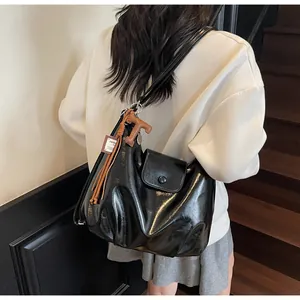 Détail du sac cabas en cuir brillant noir avec pendentif T et pompon sur un mannequin