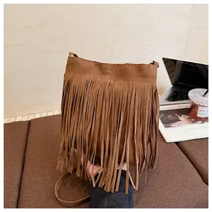 Détail d'un sac seau en daim marron avec de longues franges sur un fond en bois épuré