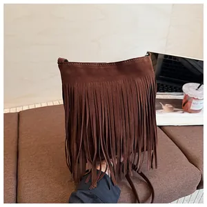Détail du sac seau en daim marron avec de longues franges dans un décor de café chic