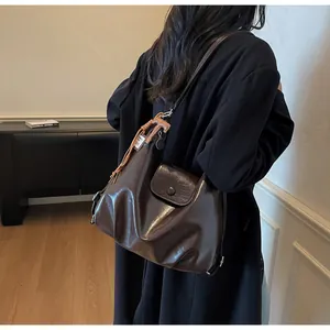 Détail d'un sac cabas en cuir marron foncé avec pompons sur l'épaule d'un mannequin