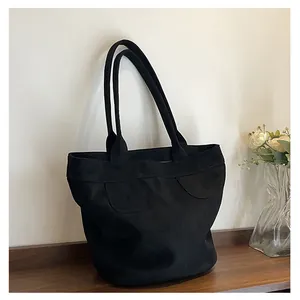 Dettaglio della borsa tote nera opaca con patta curva su superficie in legno scuro